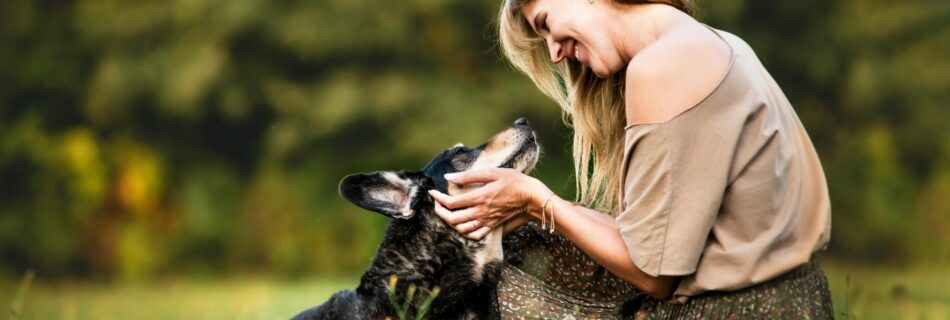Femme accroupie dans un champ caressant son chien, illustrant une relation maître chien harmonieuse et un comportement équilibré grâce aux conseils d'un éducateur canin.