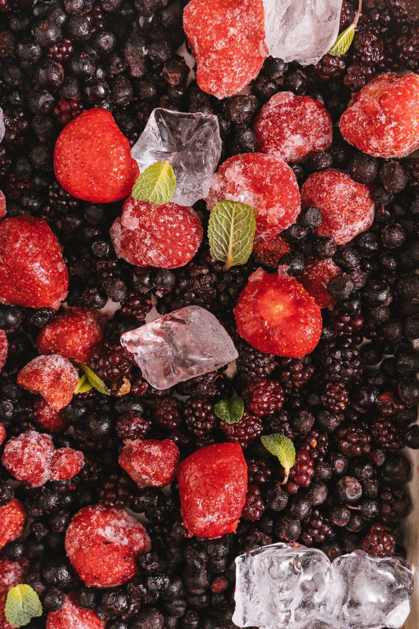 Fraises, myrtilles et mûres congelées avec des glaçons et des feuilles de menthe