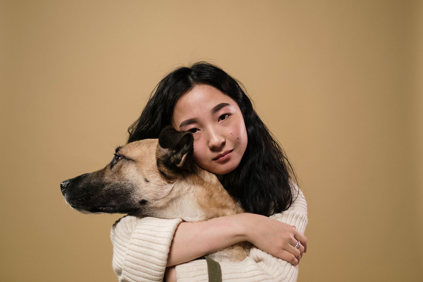 Jeune femme aux cheveux longs qui serre contre elle un chien fauve et noir, sur un fond beige