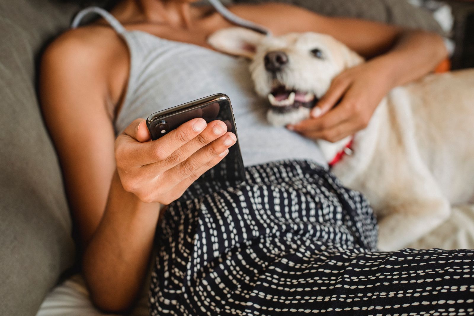 Personne allongée avec un chien clair qui se blottit contre elle, un smartphone dans la main
